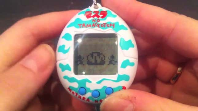 Le Mothra Tamagotchi, tenu entre deux mains.