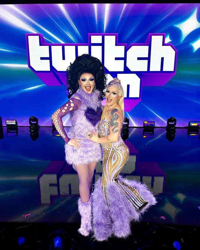 Deux drag queens au look fabuleux sourient sur une scène devant un logo de la TwitchCon.