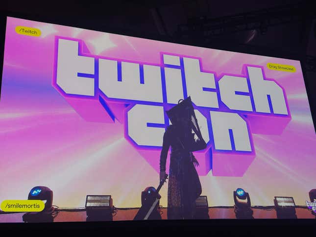 Une drag queen dont la silhouette ressemble à celle de Pyramid Head se tient sur scène devant un logo TwitchCon.